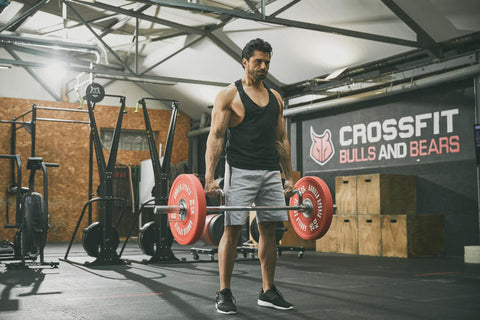En man som tränar farmers walks med skivstång och viktskivor på ett gym